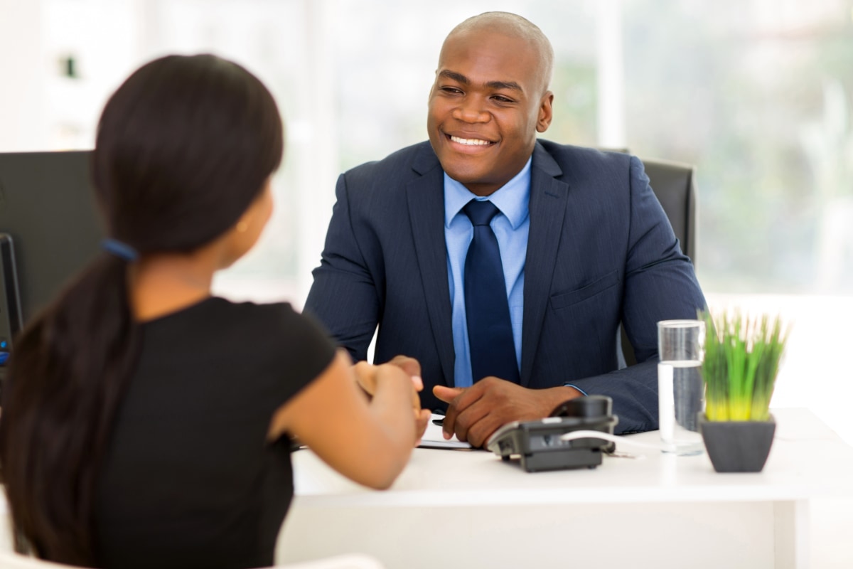 man sitting at desk shaking hands with woman