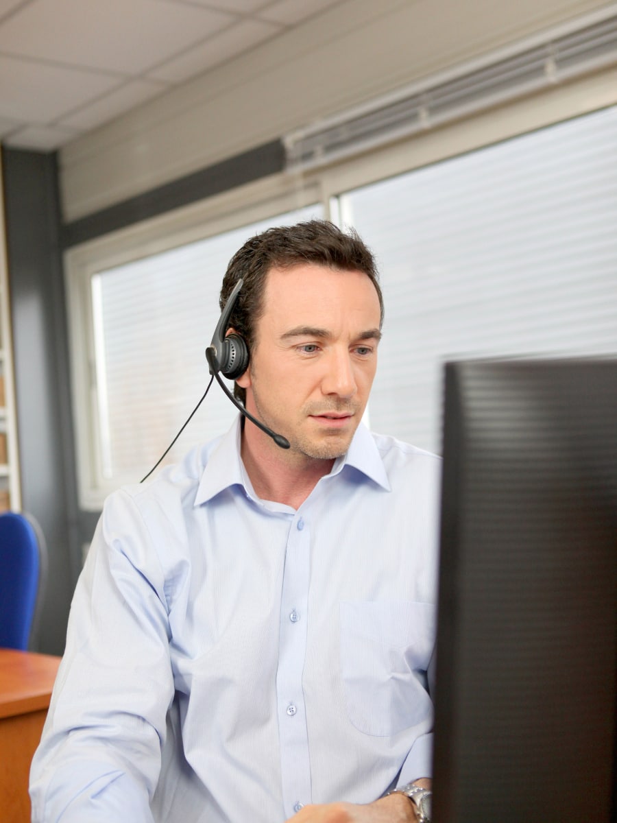 man wearing phone headset looking at computer screen