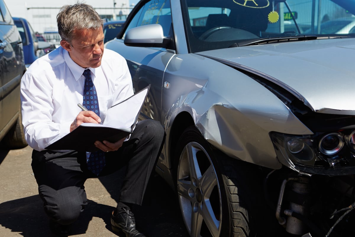 claims adjuster with notebook looking over car damage