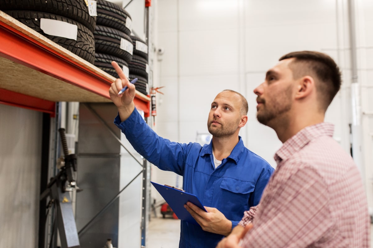 two men looking at stack of tires in mechanic garage